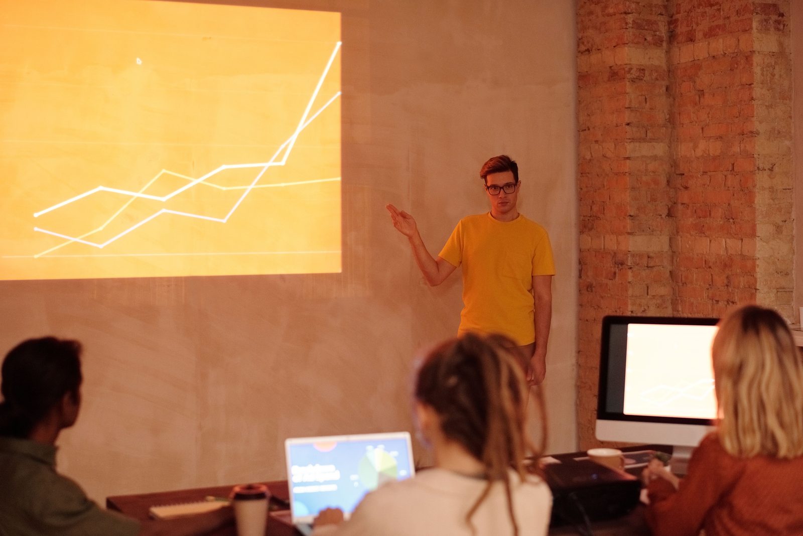 A presenter gesturing at a projected line chart in front of a small audience